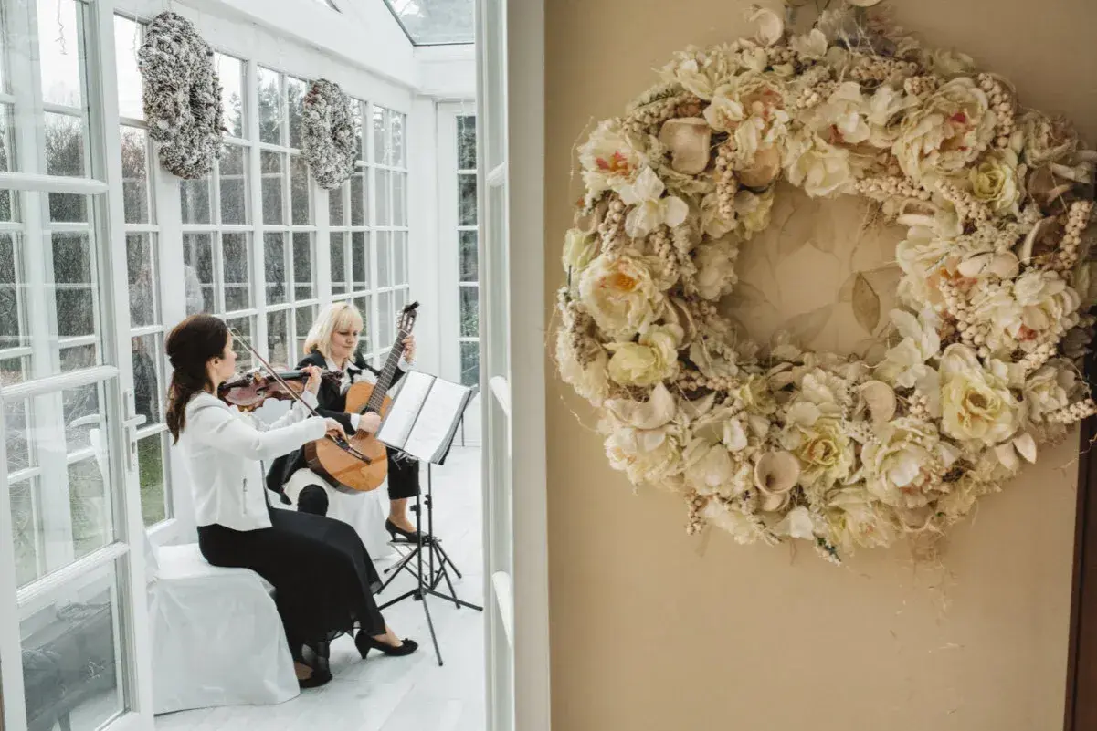 Elegancka oprawa muzyczna ślubu: skrzypaczka i gitarzystka tworzą magiczną atmosferę. Obok wianek z kwiatów.
