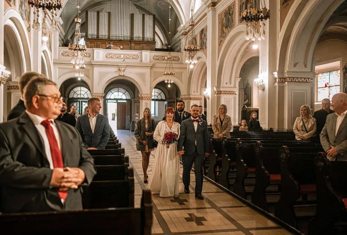 Para młoda idzie do wyjścia z kościoła, a goście śpiewają pieśń na wyjście z kościoła - ślub.