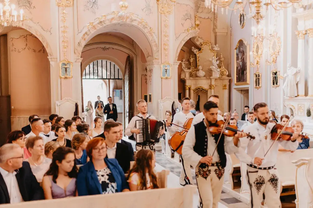 Muzycy grają pieśń na wyjście z kościoła podczas ślubu. W tle para młoda opuszcza świątynię.