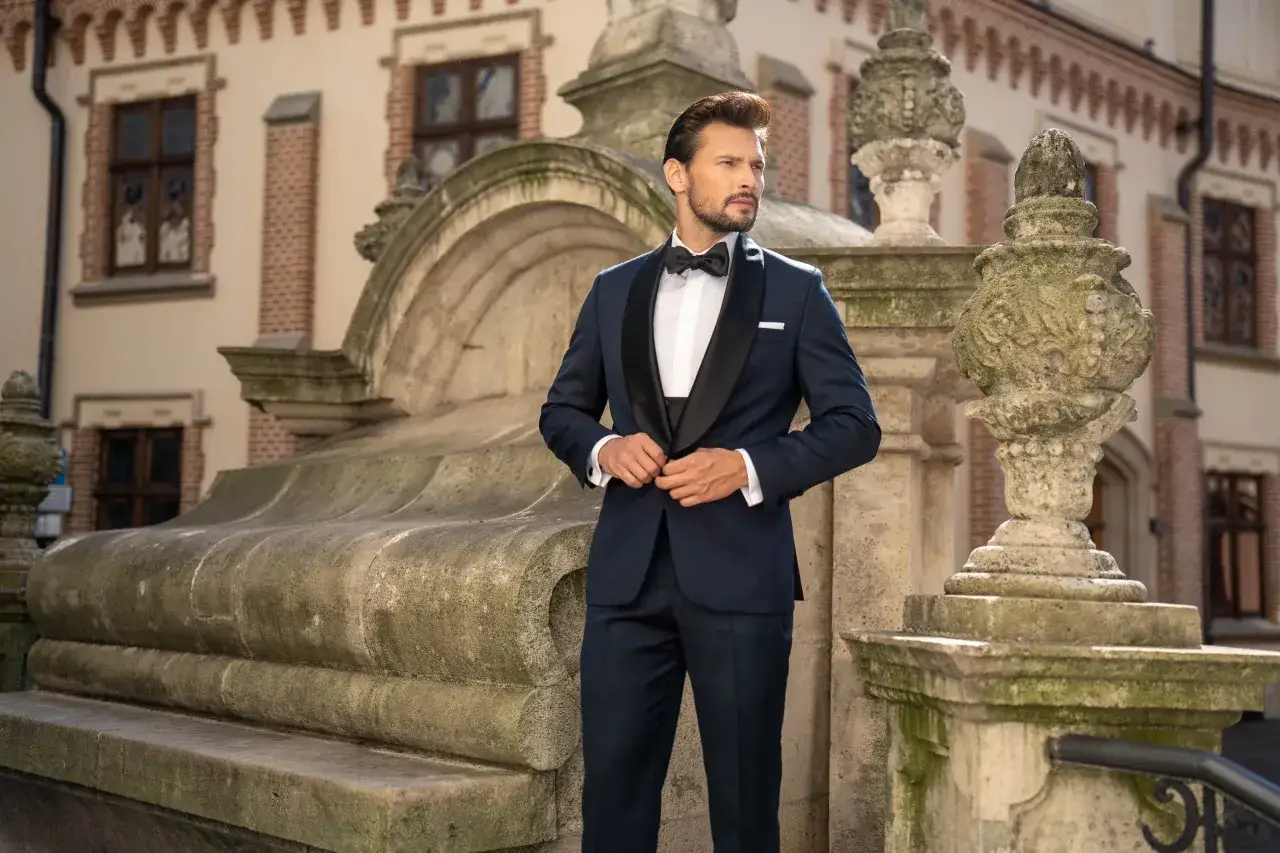 Elegancki garnitur dla niskiego mężczyzny, podkreślający sylwetkę. Klasyczny granatowy smoking z czarnymi klapami, biała koszula i czarna mucha.