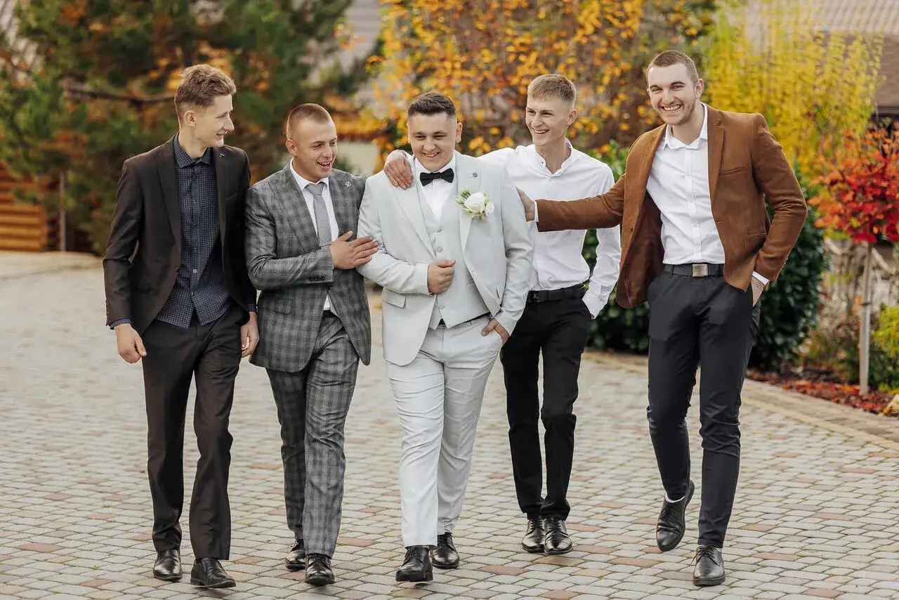 Pięciu panów w garniturach na wesele. Jasnoszary, brązowy, czarny i kratka – każdy ma swój kolor garnituru na wesele.
