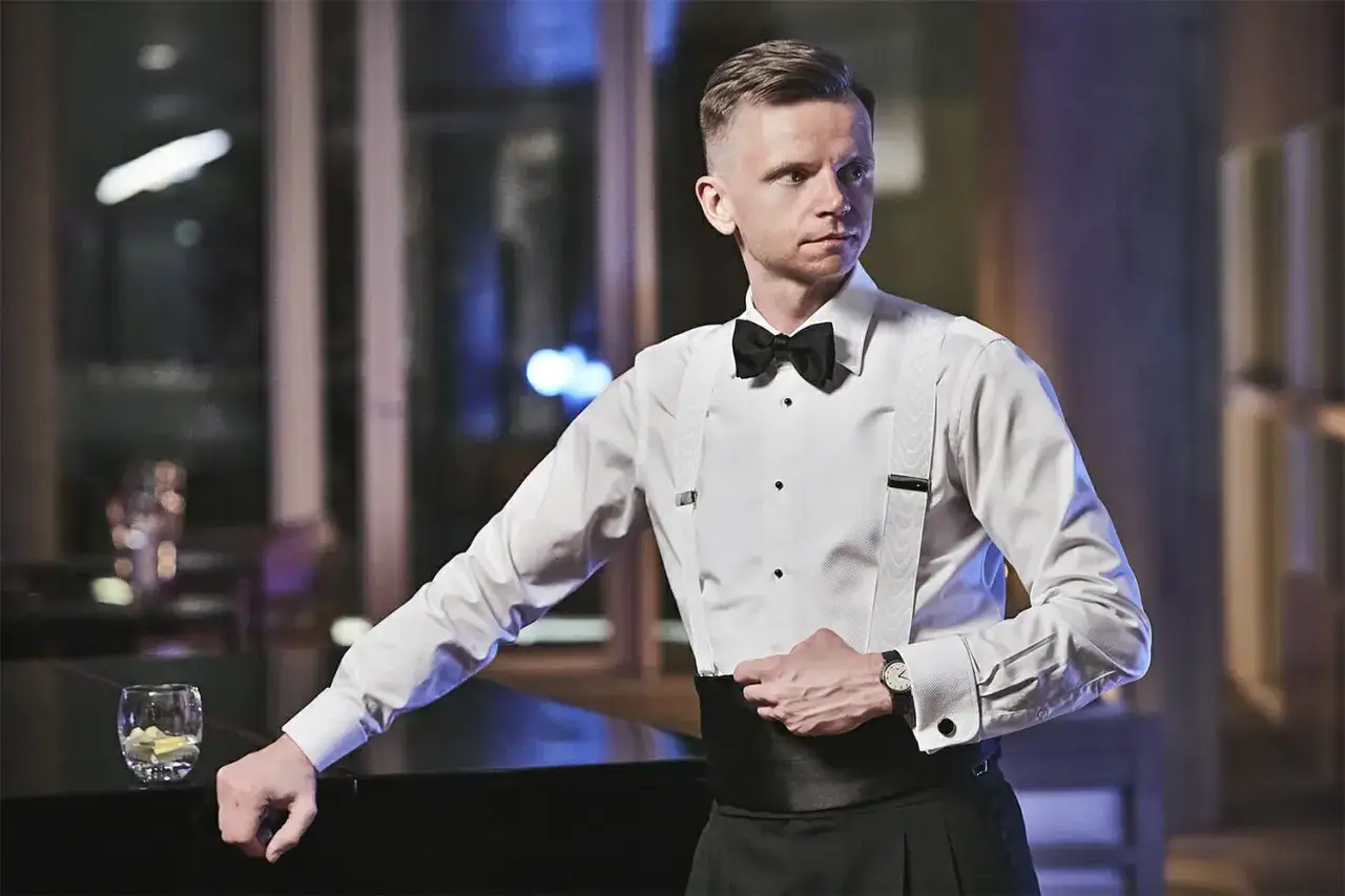 Elegancki mężczyzna w białej koszuli, czarnej muszce i szelkach, z pasem do smokingu.