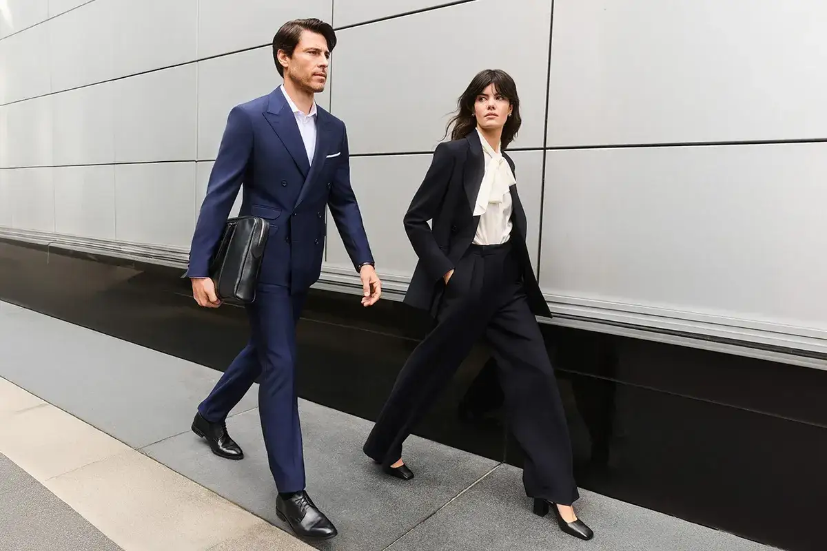 Para idąca w eleganckim business attire, mężczyzna w granatowym garniturze, kobieta w ciemnym kostiumie.