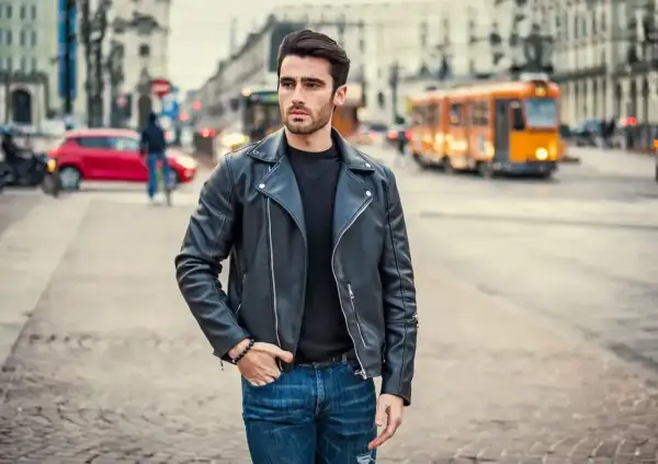 Młody mężczyzna w skórzanej kurtce i jeansach, stylizacja nawiązująca do moda męska lata 90. na tle miejskiej ulicy.
