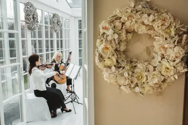 Elegancka oprawa muzyczna ślubu: skrzypaczka i gitarzystka tworzą magiczną atmosferę. Obok wianek z kwiatów.
