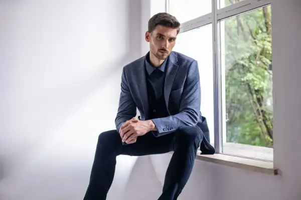 Elegancki mężczyzna w granatowej koszuli i marynarce, zastanawia się, jakie spodnie do niebieskiej koszuli będą najlepsze.