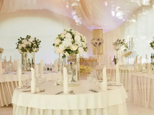 Elegancka sala weselna z białymi kwiatami i świecami. Stoły nakryte, gotowe na przyjęcie gości. Wiele pytań o szczegóły dekoracji sali weselnej.
