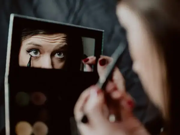 Kobieta wykonuje makijaż wieczorowy, precyzyjnie rysując kreskę eyelinerem na oku.