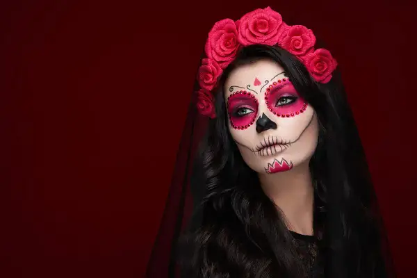 Kobieta z makijażem na halloween w stylu Catriny, ozdobiona czerwoną opaską z róż i welonem.